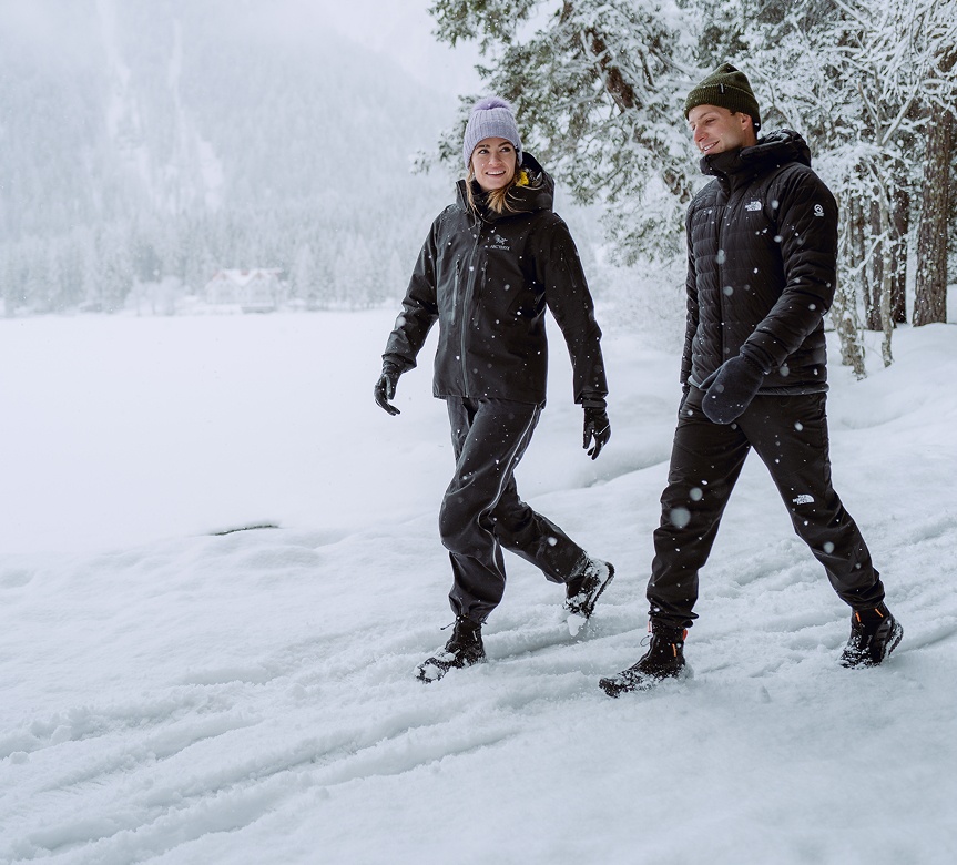 Zwei Erwachsene spazieren durch verschneite Winterlandschaft mit Reusch Handschuhen.